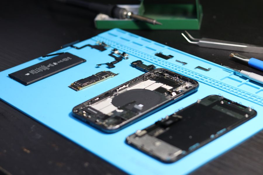 Zerlegtes Smartphone mit Werkzeug auf einer blauen Reparaturmatte
